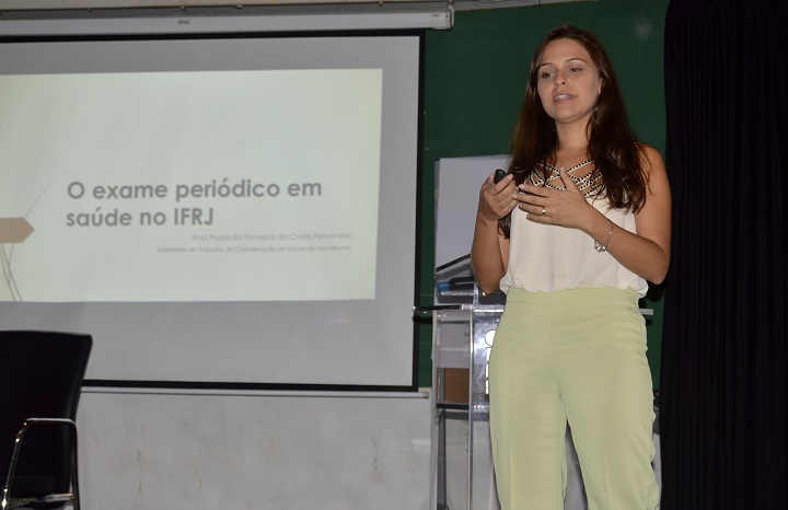 Ana Paula da Fonseca fala com o público, de pé no palco do auditório, com apresentação de slides ao fundo