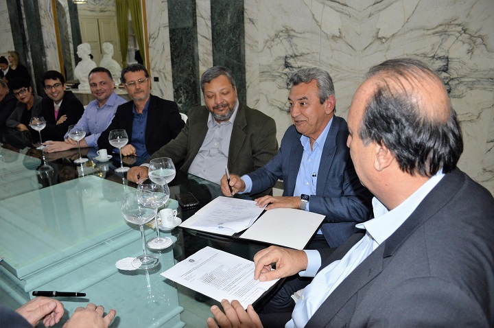 Autoridades presentes sentados ao redor da mesa, conversando, após assinatura do termo de cessão