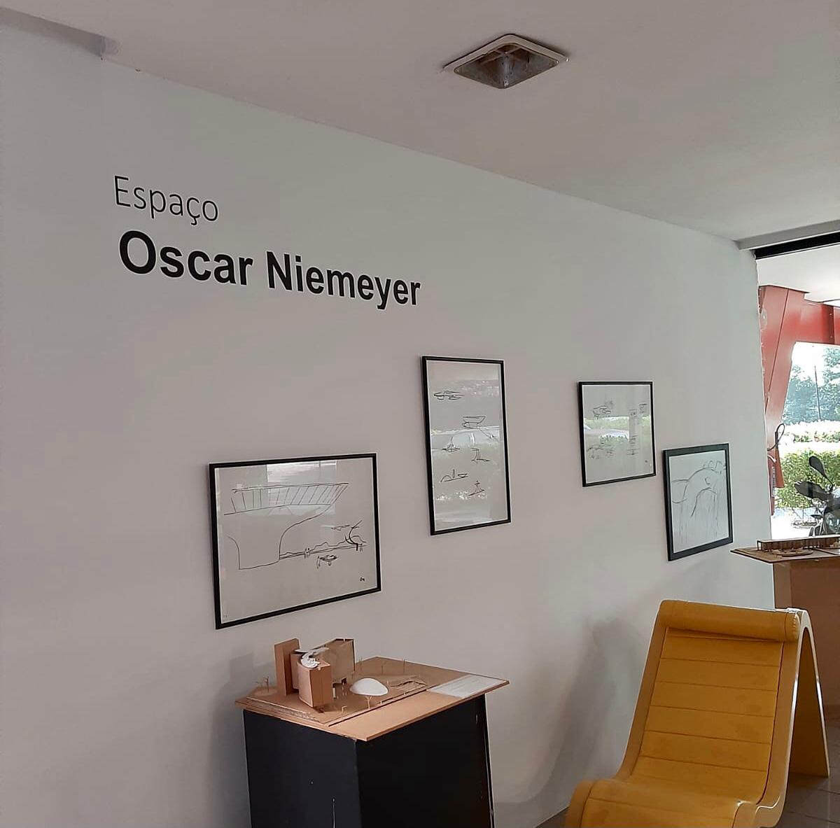 parede branca, tres quadros pequenos com desenhos de Oscar Niemeyer. ao fundo aplacapequena com os dizeres "espaço Niemeyer"