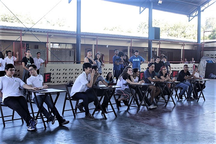 alunos divididos em equipes e sentados ao redor de mesas