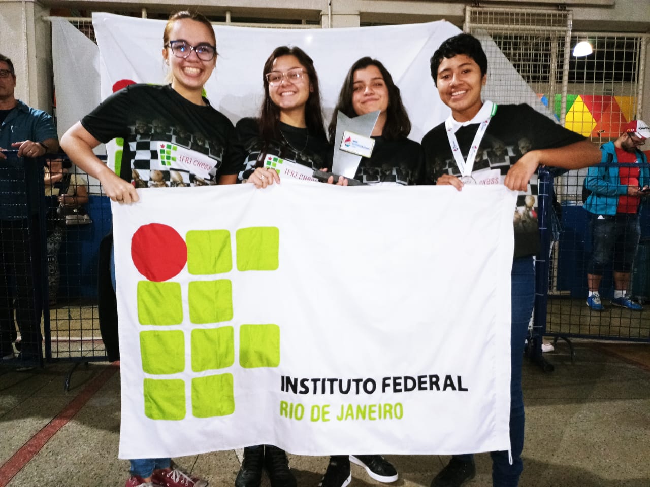 quatro alunos sorrindo seguram a sua frente uma bandeira do IFRJ