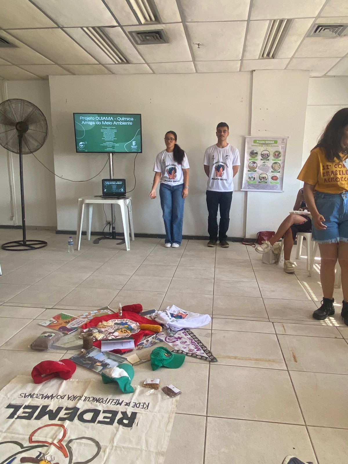 estudantes do campus apresentando projeto no congresso em uma sala com objetos no chão