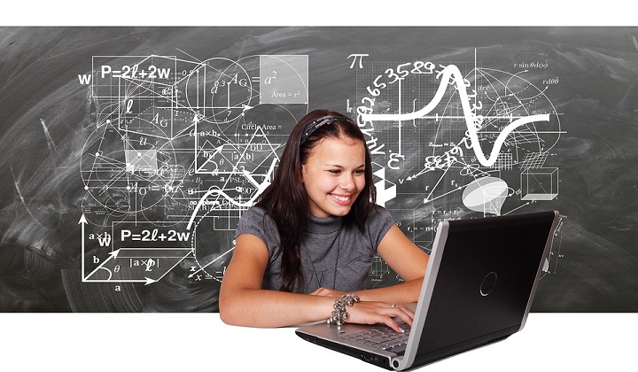 menina sorrindo de frente para o computador , com um quadro de giz atras com fórmulas matemáticas 