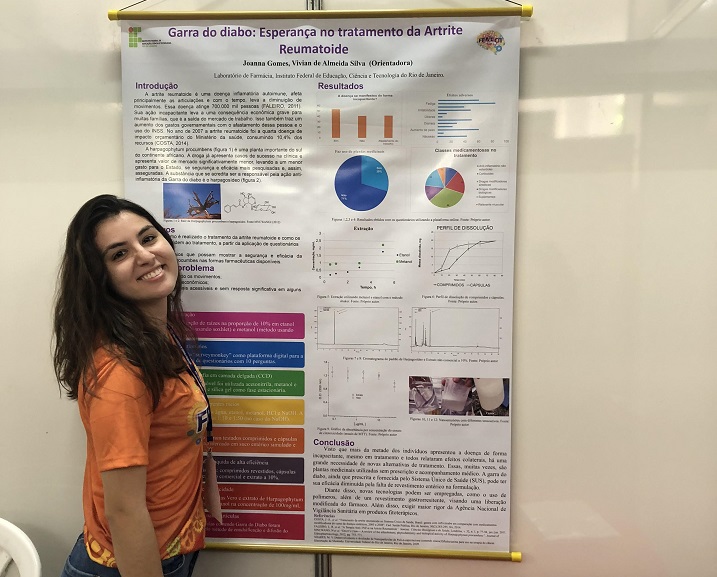aluna Joanna Gomes posando para foto com o banner de seu projeto na FENECIT