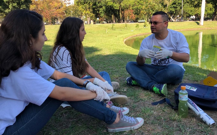 estudante italiana sentada na grama conversando com outra aluna e o professor 